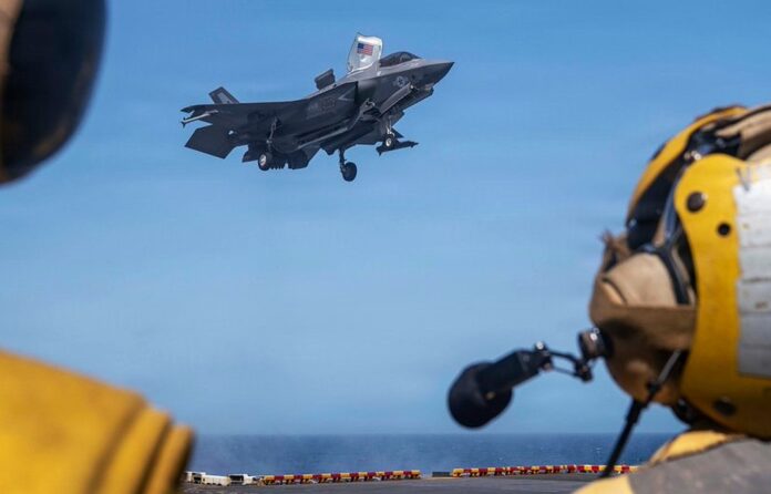 US Sailors observe as a Marine Corps F-35B stealth fighter lands on the deck of USS Tripoli (LHA 7)